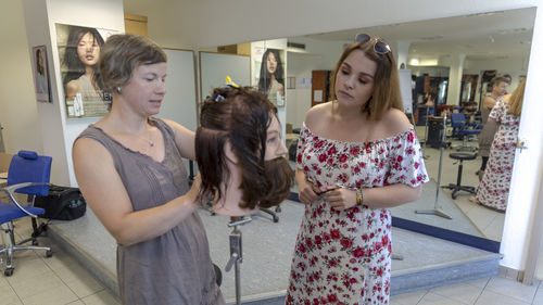 Ausbilderin zeigt Friseurlehrling Haarschnitttechniken an einem Puppenkopf