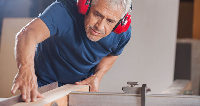 Älterer Mann mit Gehörschutz am Kreissäge