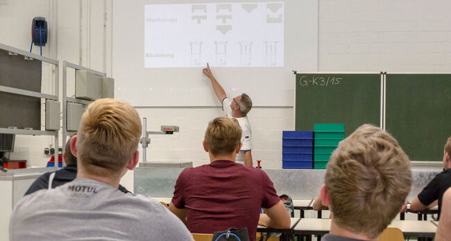 Schüler schauen vor zur Tafel. Lehrer erklärt etwas.