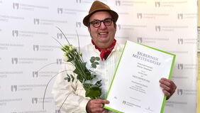 Ein Drechslermeister hält seinen Silbernen Meisterbrief und Blumen in der Hand.