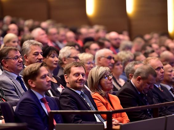Ministerpräsident Michael Kretschmer sitzt im Publikum und lächelt in die Kamera.