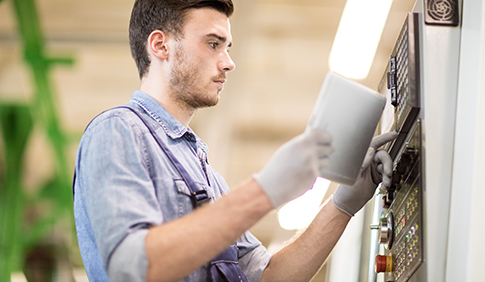 Ein junger Mann in Arbeitskleidung und mit Arbeitshandschuhen bedient eine technische Anlage.