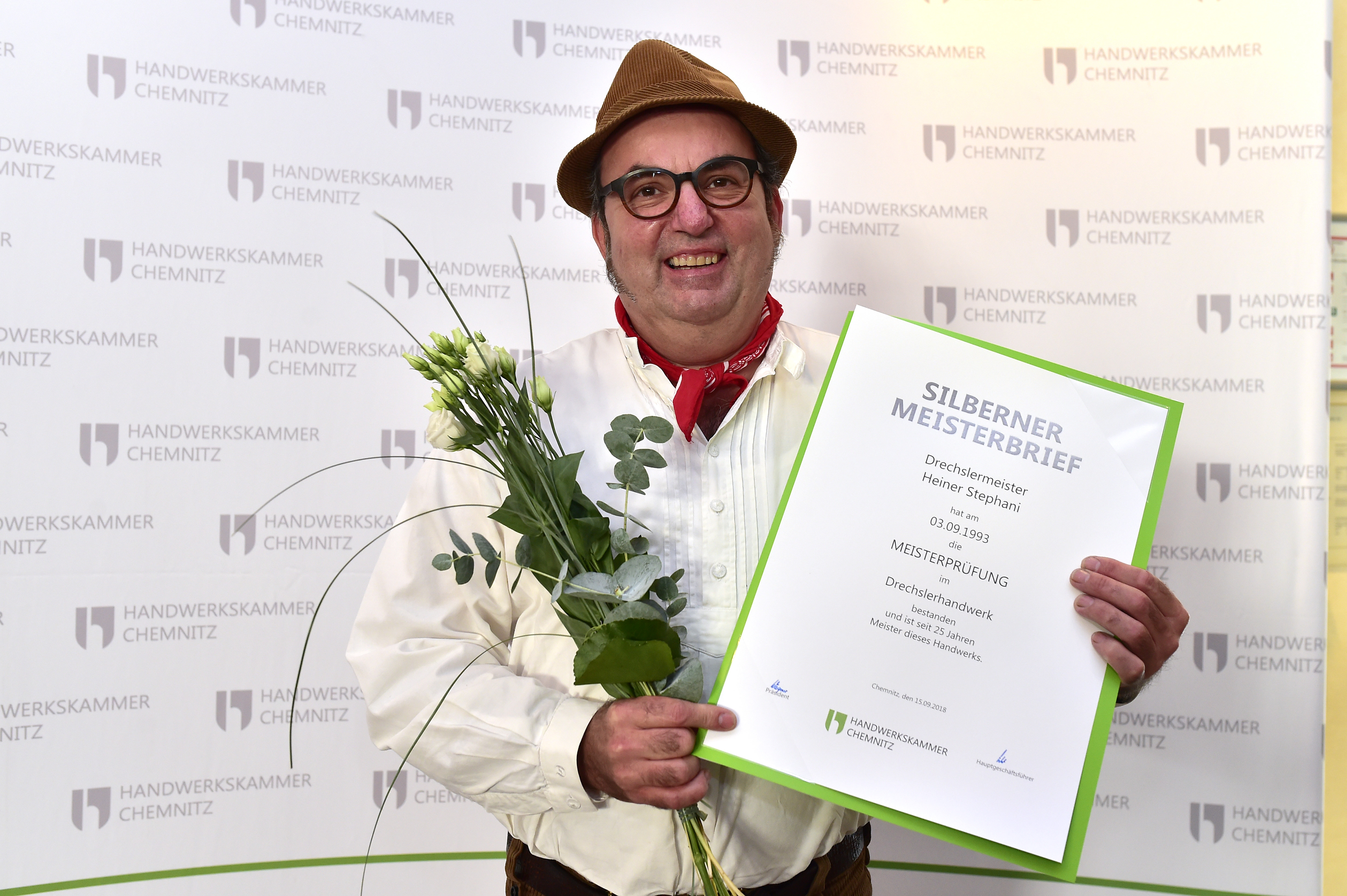 Ein Drechslermeister hält seinen Silbernen Meisterbrief und Blumen in der Hand.