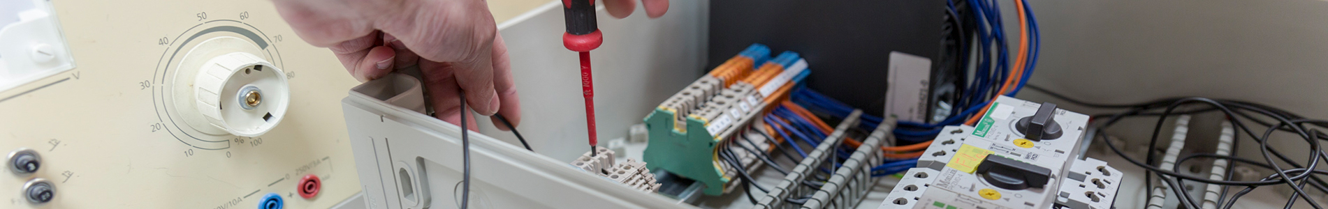 Das Bild zeigt eine Ausbildungssituation in der Elektroausbildung. Ein Auszubildender verdrahten mit einem Schraubendreher einen Schaltschrank.